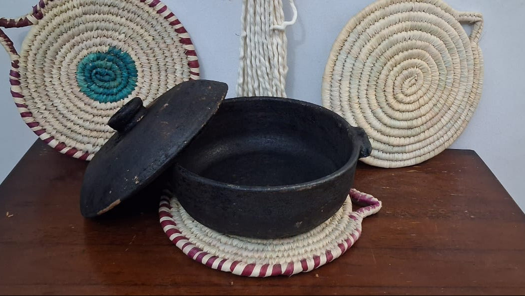 Black pot , surrounded by woven baskets on a wooden surface.